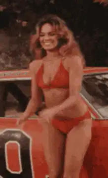 Bo Derek posing in red bikini by car
