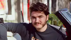 Man with mustache leaning on car