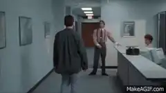 Man in hallway adjusts tie after passing another man