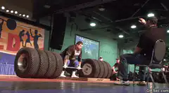 Man lifting heavy tire barbell on stage