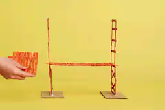 Hand building a bridge with orange popsicle sticks