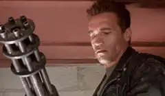 Arnold Schwarzenegger looks at minigun then smirks