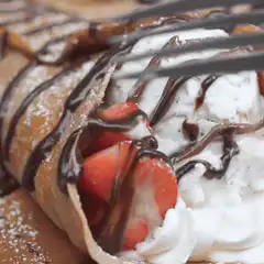 Fork cutting into crepe with strawberries and cream