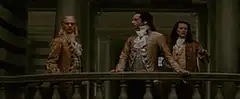 Three men in 18th century coats on a balcony