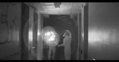 Two figures in a hallway with a bright light