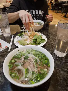 Person adding bean sprouts to pho