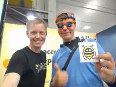 Two men at a convention holding a bee sticker