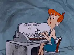 Wilma Flintstone typing on a stone typewriter