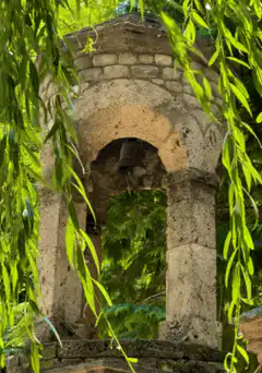 Bell in stone archway behind willow leaves