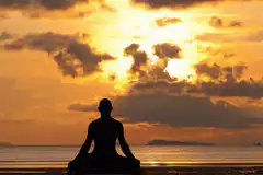 Silhouette meditating on beach at sunset