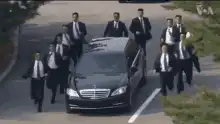 Men in suits running around a limo