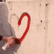 Hand spray painting a red heart on a wall