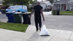 man throws trash bag into bin