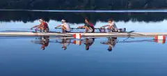 Four men rowing a boat on calm water
