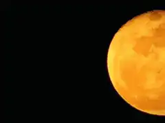 Orange moon moves across black sky