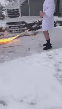 Man in bathrobe drinks wine while fire burns in snow