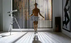 Shirtless man jumping rope in sunlit room