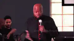 Bald man in black shirt raises hand while speaking