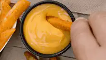 Hand dipping cheese stick in cheese sauce