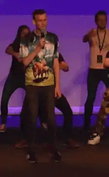 Man in Hawaiian shirt sings on stage with dancers
