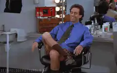 Seinfeld sitting in a chair with one leg up