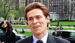 Willem Dafoe smirking in a park