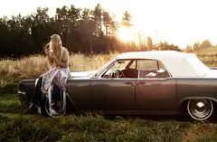 Woman sitting on vintage car at sunset