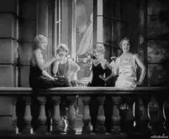Four women in flapper dresses toasting on a balcony