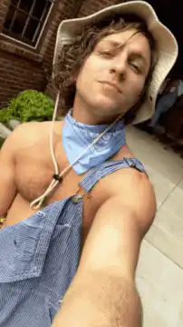 Man in overalls and hat smiling selfie