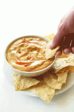 Hand dipping tortilla chip in queso