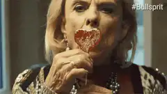 Old woman eating heart lollipop and man watching