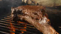 Tomahawk steak grilling over flames
