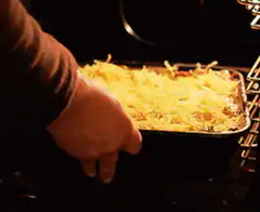 hand putting cheesy casserole in oven
