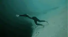 diver swimming underwater near cliff