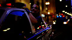 Officer leaning on police car at night