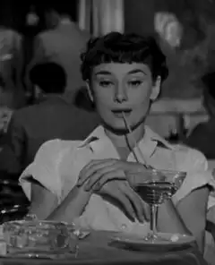 Audrey Hepburn sips a drink and smiles