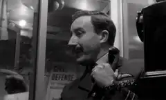 Man adjusting tie with Civil Defense poster