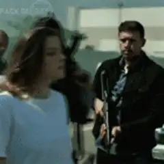 Woman in white shirt walking past armed men