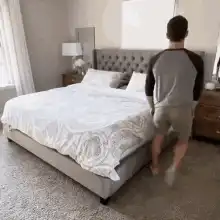 man jumps on bed with blanket