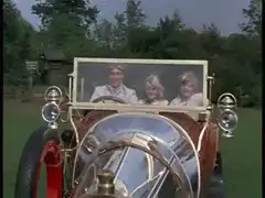 Three people in a vintage car with Japanese subtitles