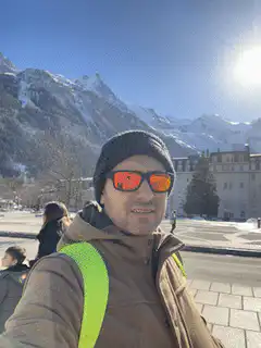 Man in beanie and sunglasses smiling in front of snowy mountains