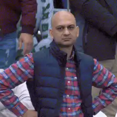 Bald man in plaid shirt and vest looks around