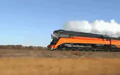 Orange steam train moving through field