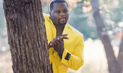 Man in yellow suit peeking from behind tree