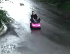 Man in pink toy car slides down wet road
