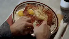 hands breaking bacon on breakfast plate