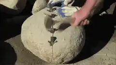 Splitting a large rock with wedges and hammer