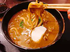 Chopsticks lifting udon noodles from curry soup