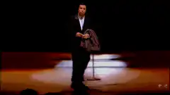 Comedian walks across stage holding jacket