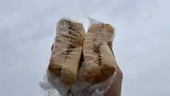 hand holding two wrapped sandwiches